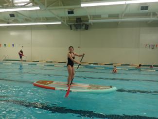 a girl standing on top of a paddleboard in the middle of an indoor swimming pool