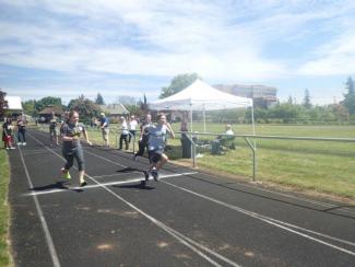 2 students running on the track with a field behind and blue skies with some clouds